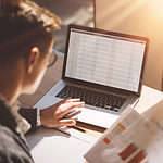 Young banking finance analyst in eyeglasses working at sunny office on laptop while sitting at wooden table.Businessman analyze stock reports on notebook screen.Blurred background,horizontal.