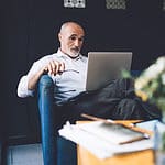 A wide view image of a man sitting while looking at his laptop.