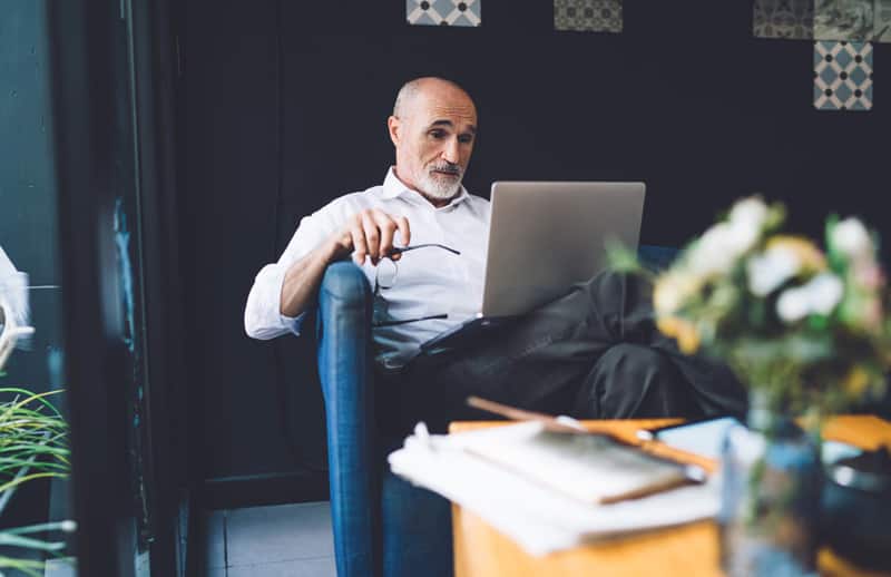 A wide view image of a man sitting while looking at his laptop.