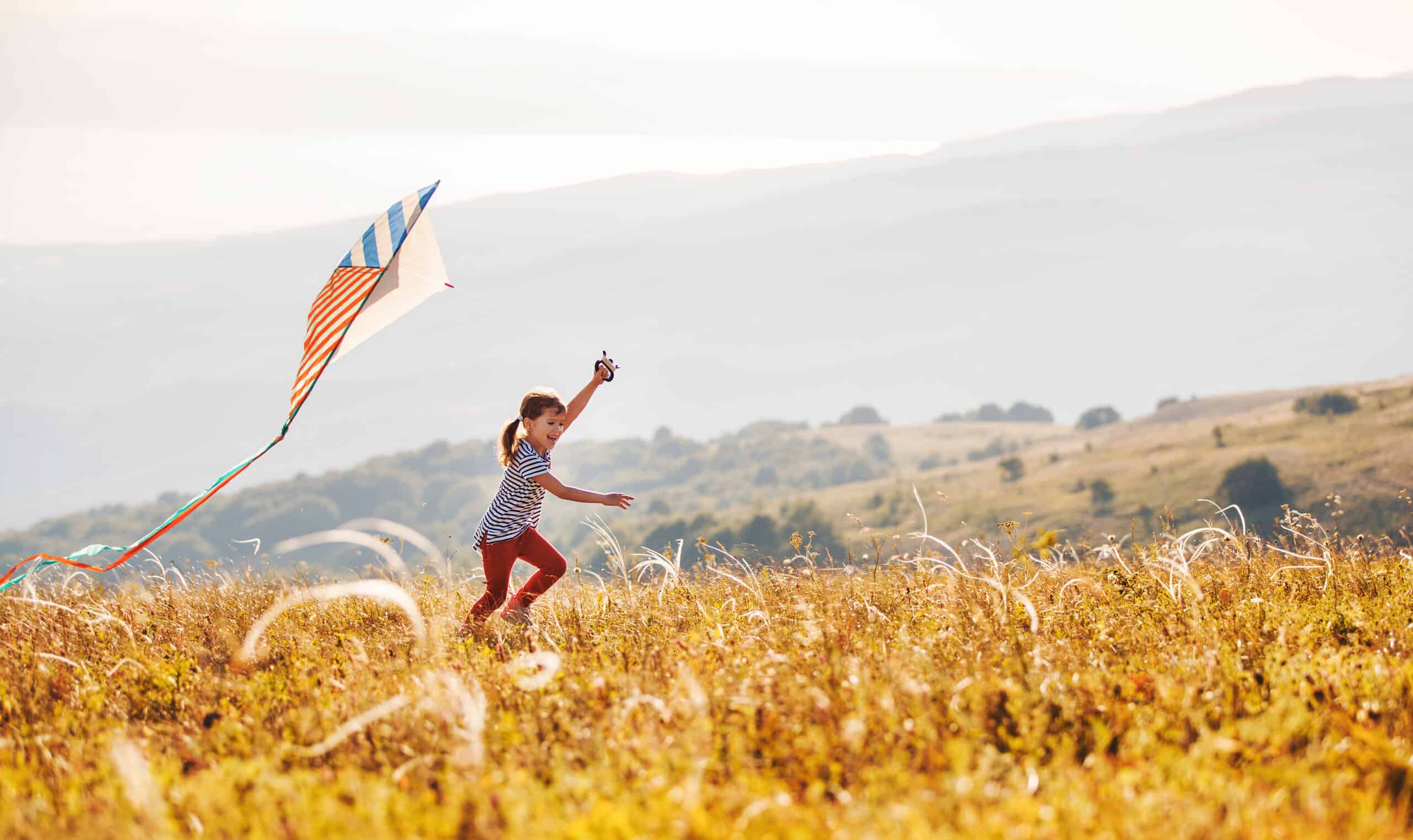 Happy child girl running with kite at sunset outdoors.