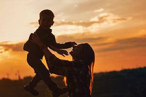 Silhouette young mother with pleasure spending time with kid in park.