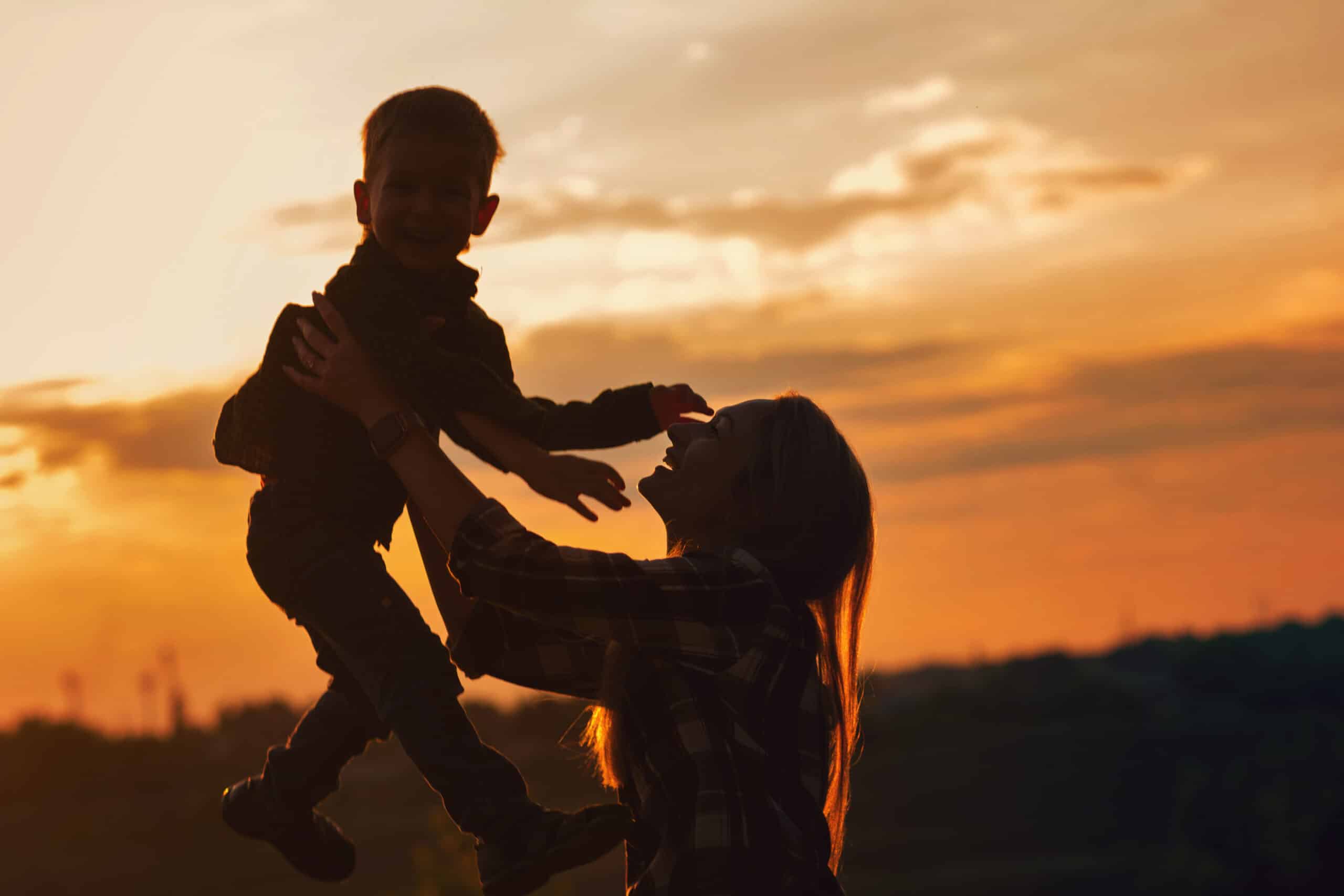 Trust Services Silhouette young mother with pleasure spending time with kid in park. Lovely Mommy throw up son against sunset. Happy childhood moments, having fun together. Enjoying life.